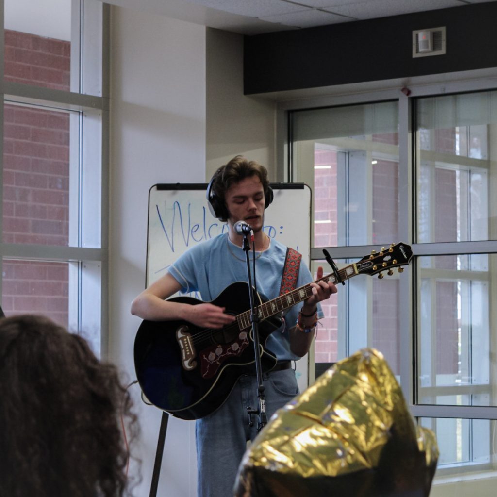 A solo singer performs a song while playing a guitar and singing into a microphone.