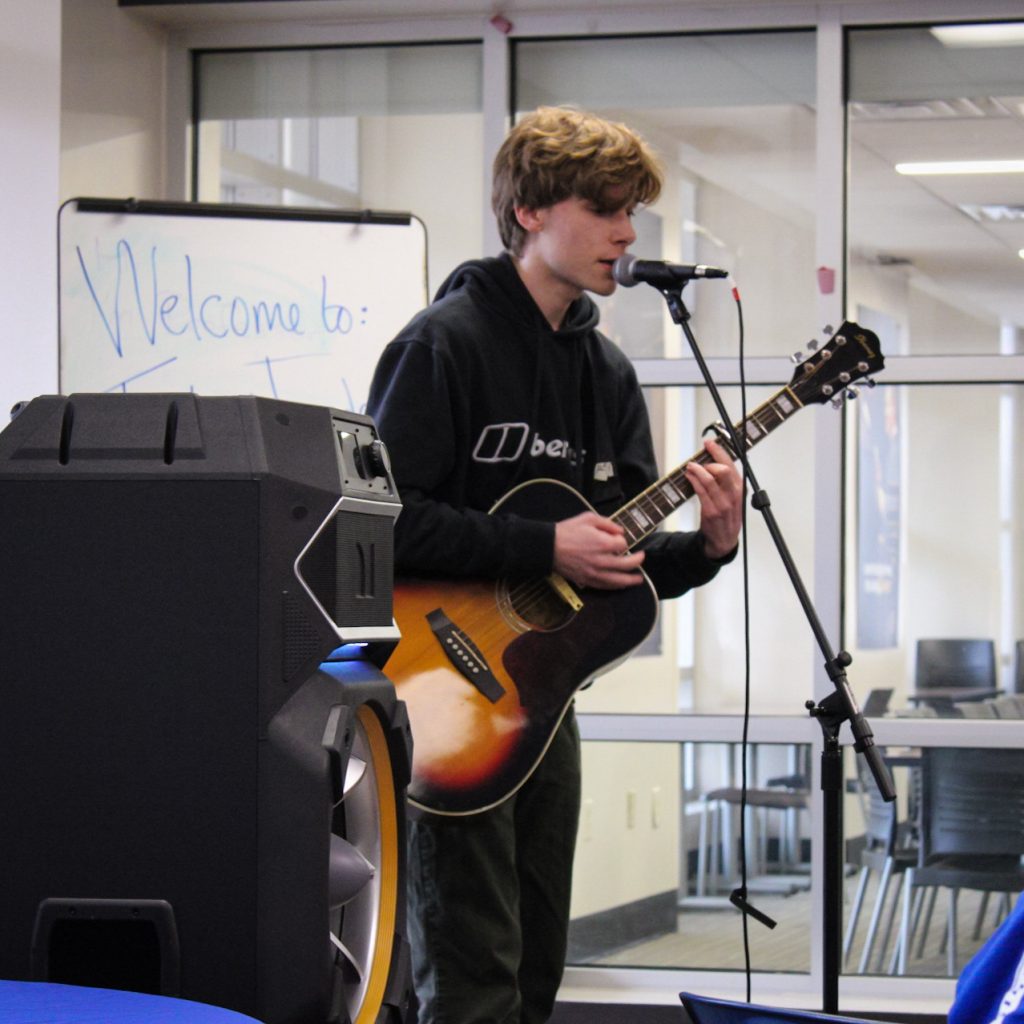 A solo singer performs a song while playing a guitar and singing into a microphone.