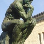Paris' Thinking Man Sculpture; image of a bronze statue of a naked man with his hand on his chin and his elbow on his knee seemingly deep in thought.