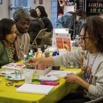 A group of students sitting at a table painting and enjoying the event.