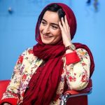 Woman sitting down on red chair in a floral shirt and red headscarf, with a blue background.