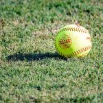 A yellow softball sitting in the grass