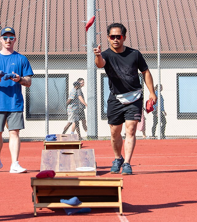 A man throwing a fabric beanbag into a cornhole board