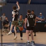A basketball team in black jerseys try to get the ball from a player in a green jersey.