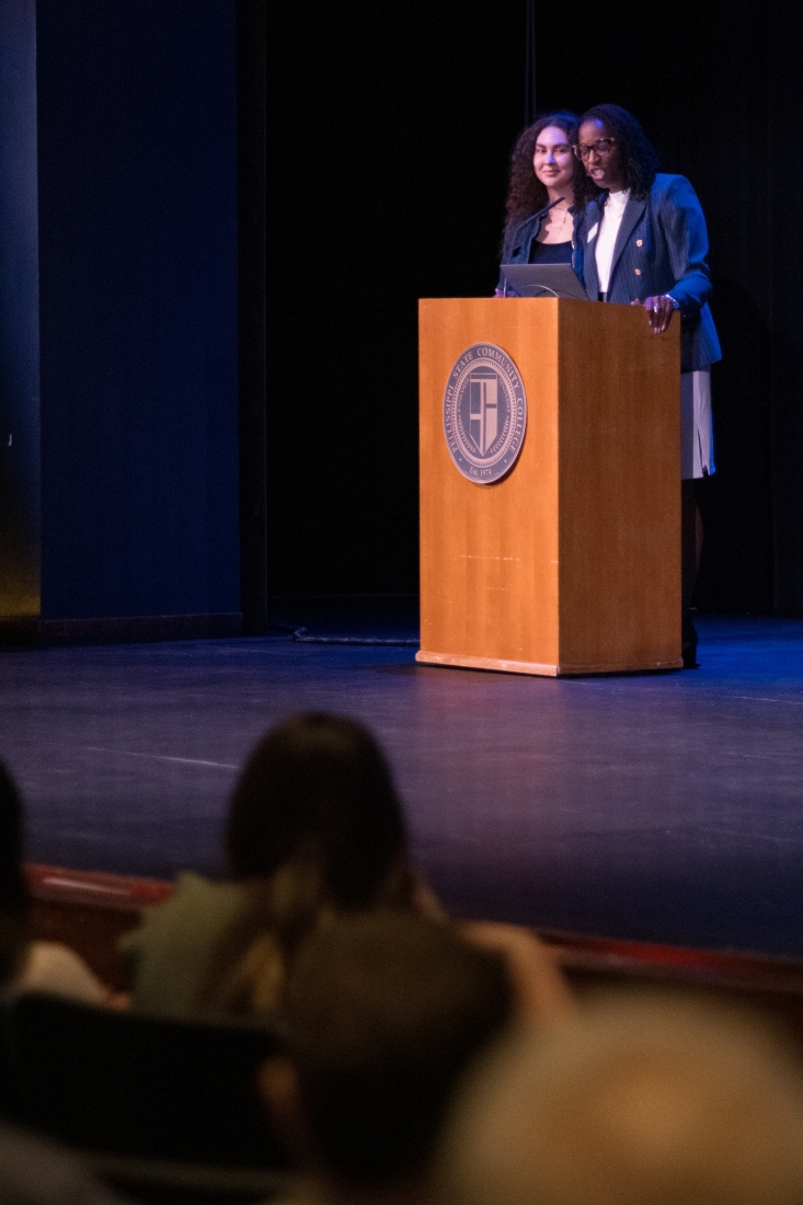 Two women stand at a podium to speak to a crowd.