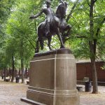 Statue of Paul Revere in a park with green trees.