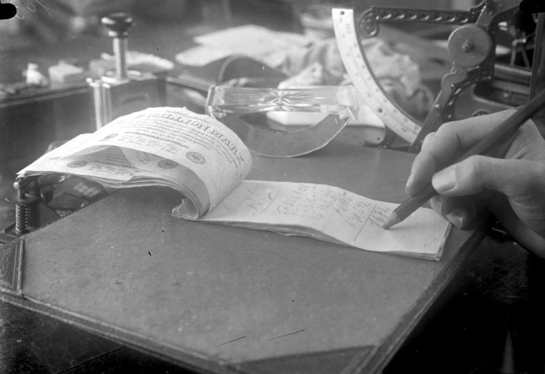 A German million-mark note with handwritten list and a hand holding a pencil.