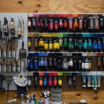 A peg board holding rows of acrylic paint tubes and brushes.
