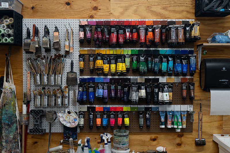 A peg board holding rows of acrylic paint tubes and brushes.