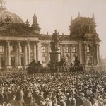 Crowd in front of a building surrounding a statue.