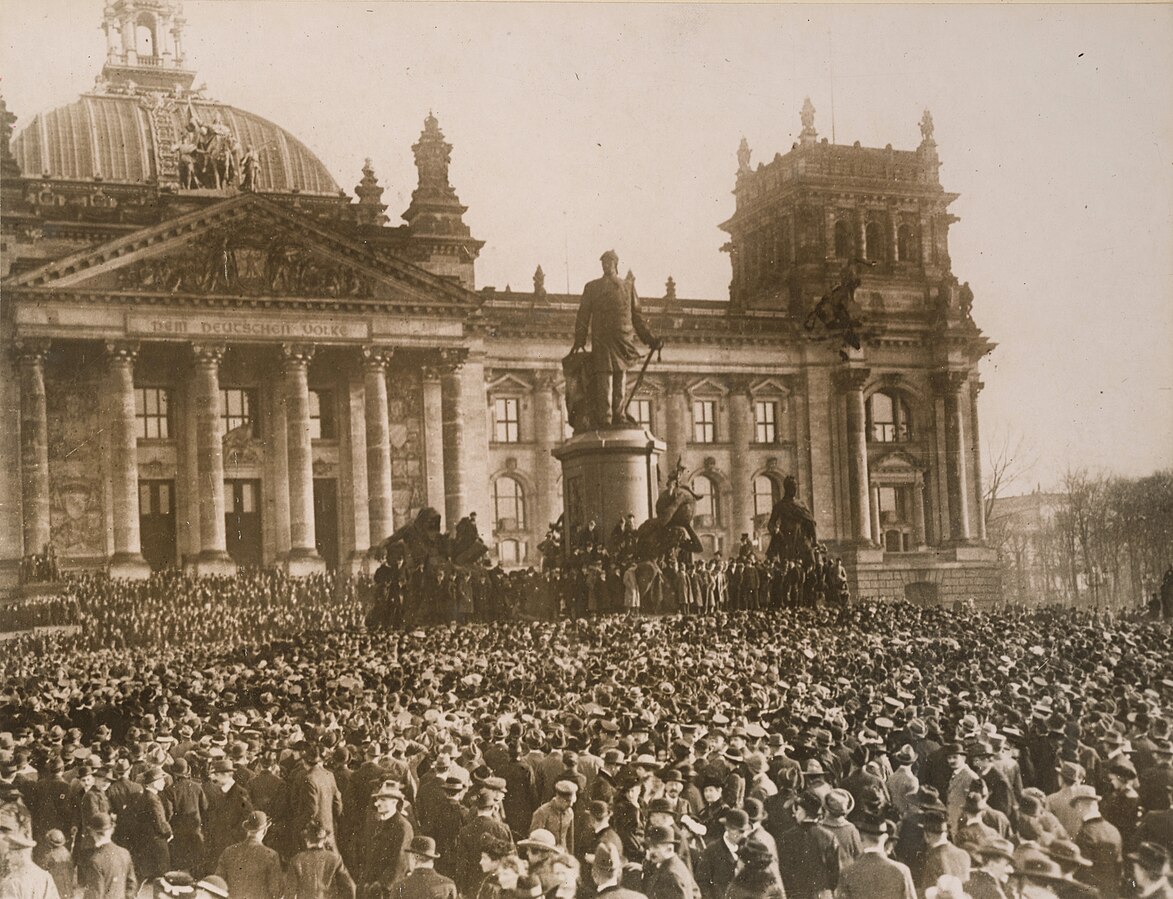 Crowd in front of a building surrounding a statue.
