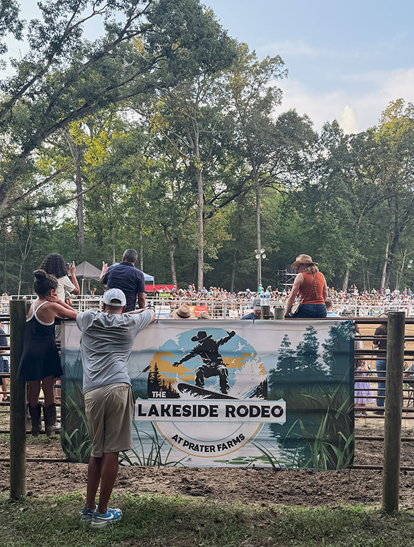 The welcome sign for the Lakeside Rodeo with attendees climbing/sitting on the gate