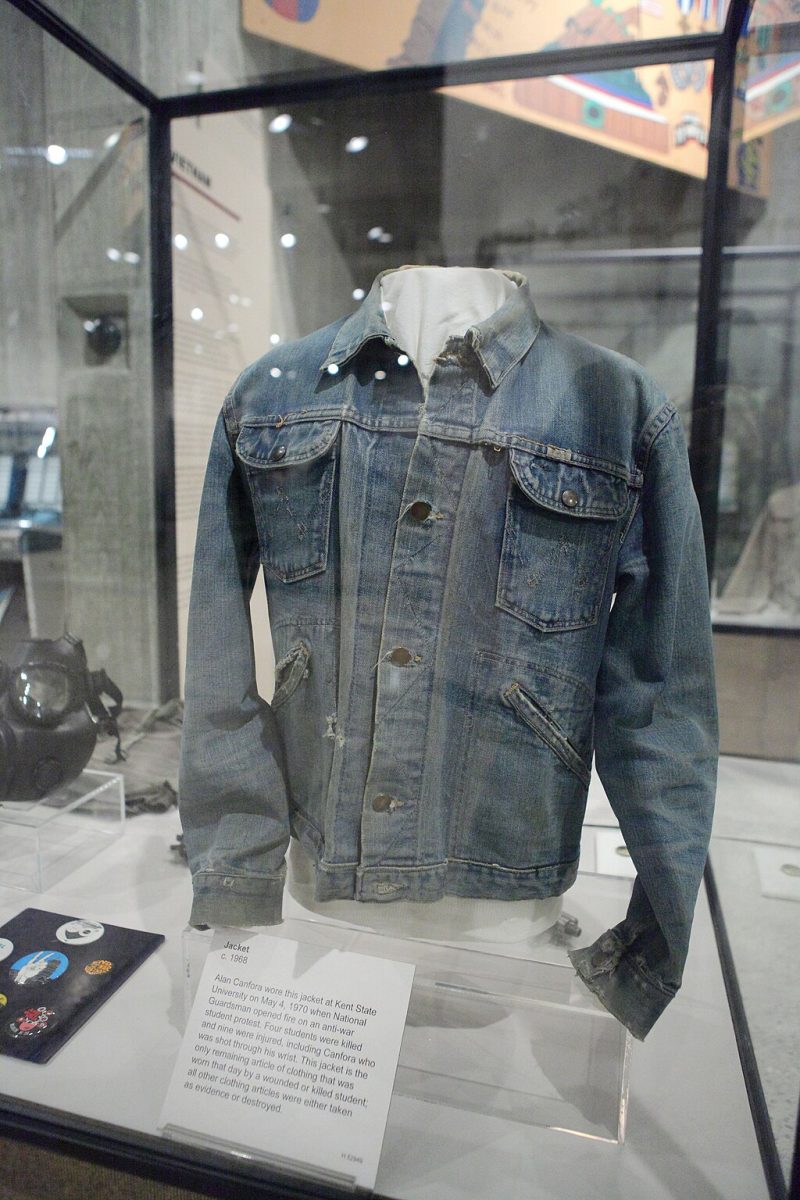 a tattered jacket on display in a museum with a description on the bottom