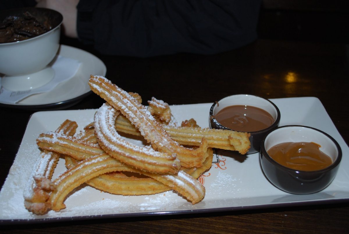 A rectangular plate of churros dusted with powdered sugar, and two small dipping bowls of chocolate and dulce de leche