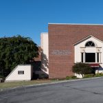 brick building with a tree and flag pole beside of it, with the name outside of it