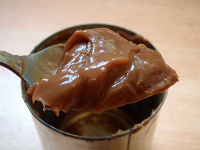 A can of a caramel-like substance with a spoon holding some above it