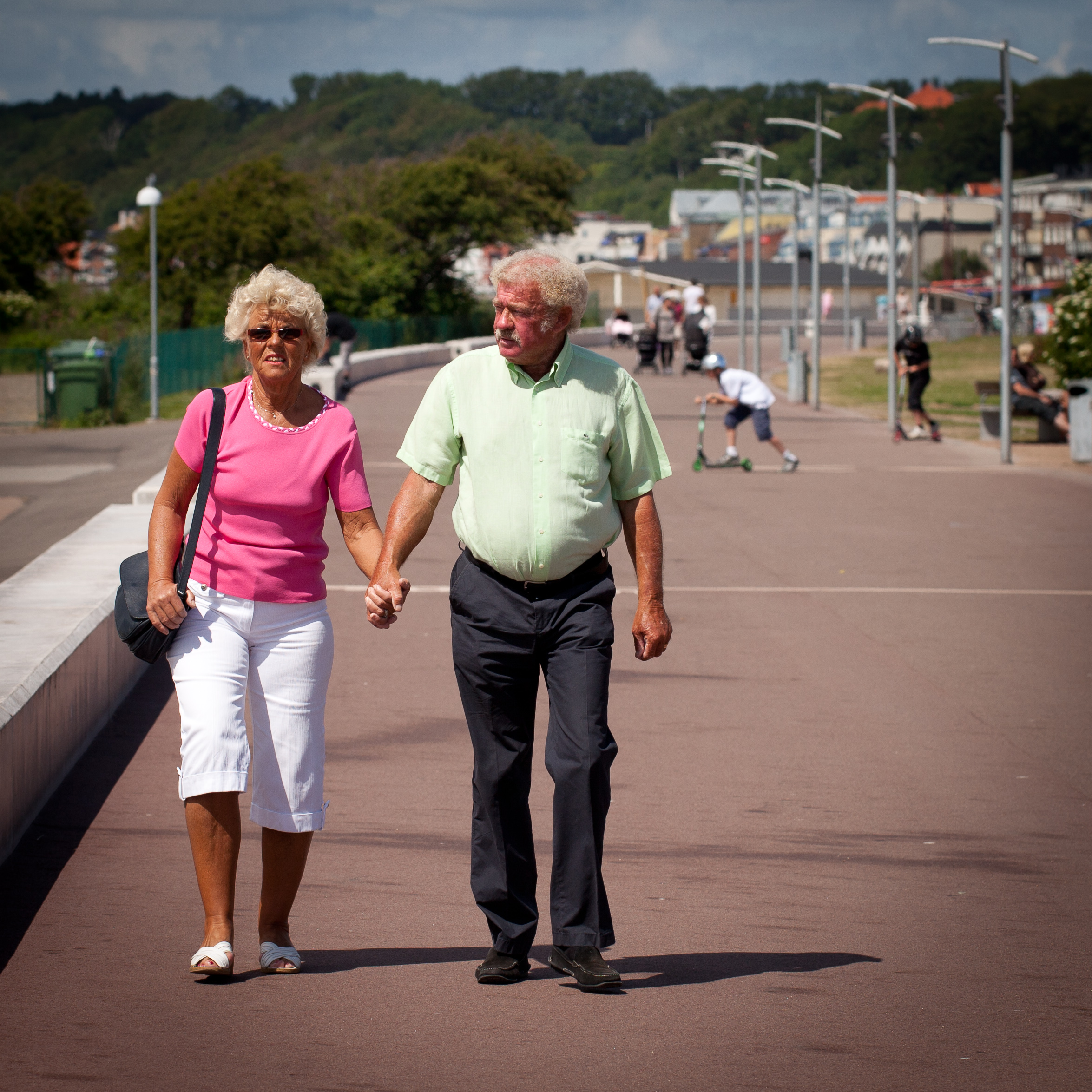 Elderly couple walks hand in hand down a busy street.