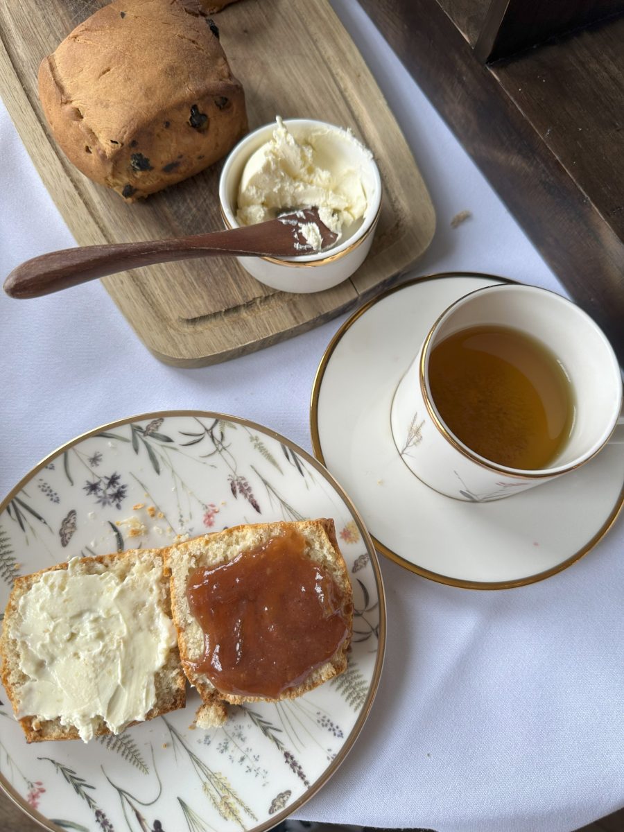 A plate of scones, a cup of tea, and bread with butter next to it.