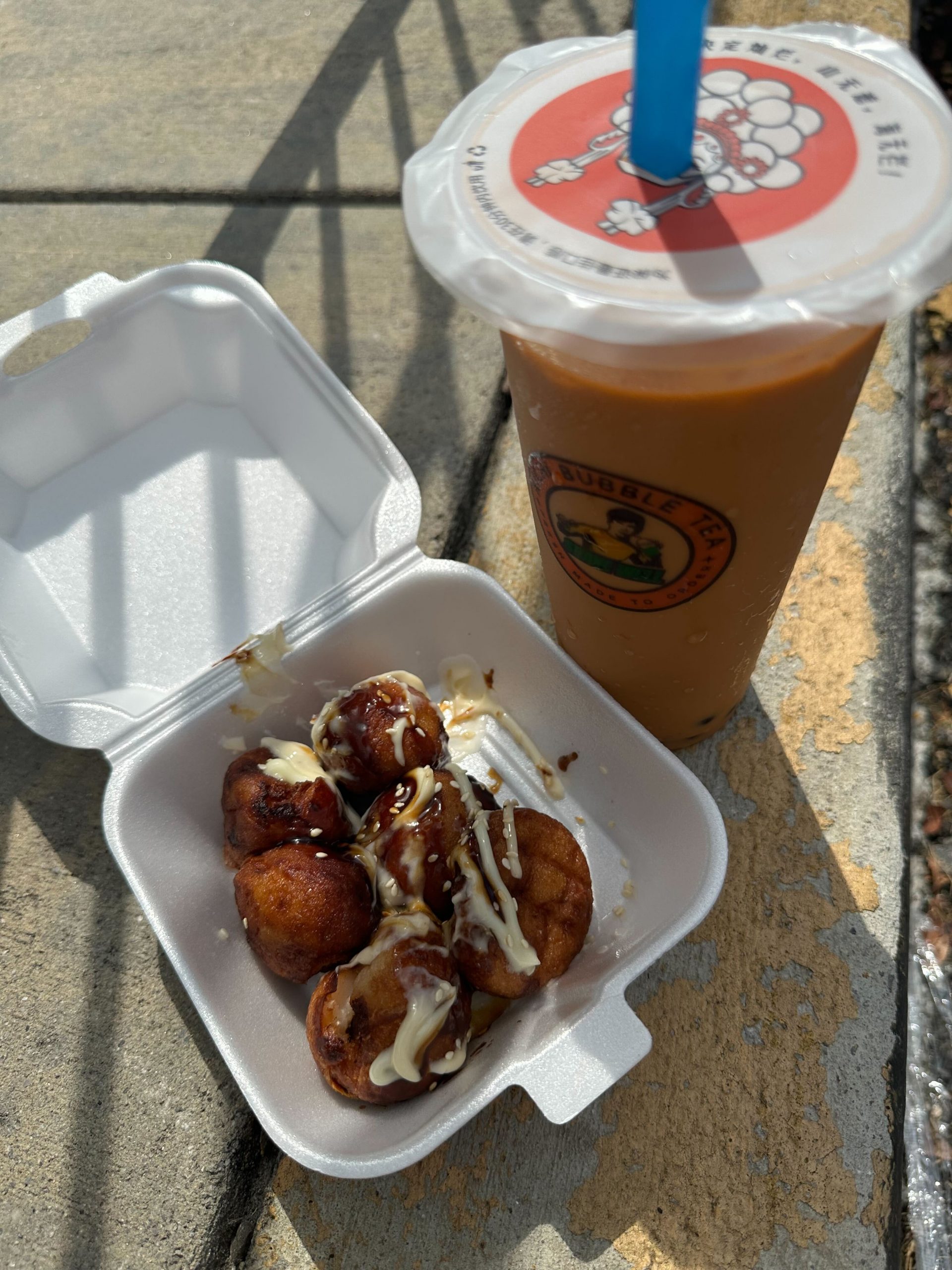 A styrofoam package with fried dough balls and a drink with a straw.