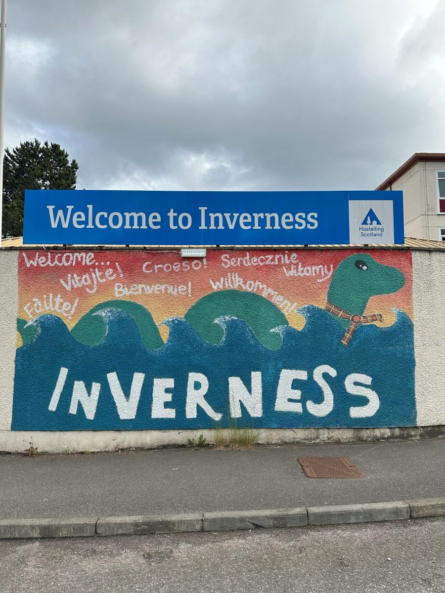 A sign that says "Welcome to Iverness. The mural below it features Nessie the Loch Ness and the word "Welcome" in various languages.