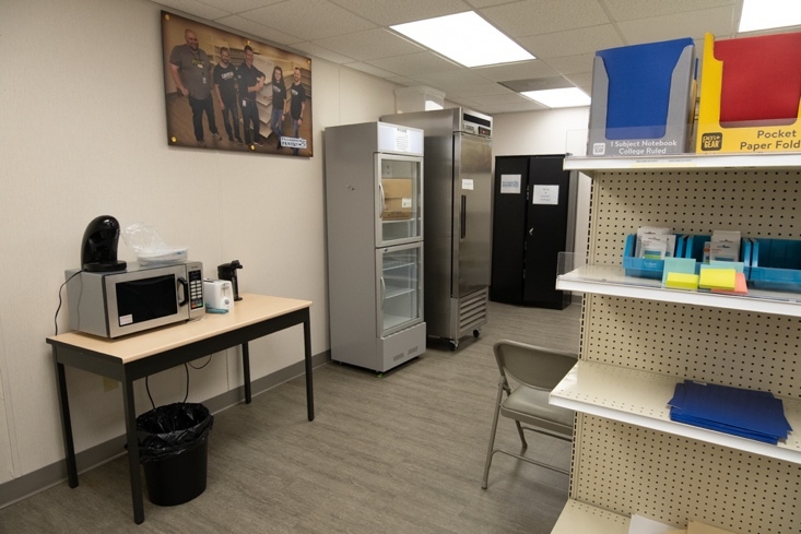 Several kitchen appliances are positioned against the wall. The opposite shelves contain school supplies and other miscellaneous items.