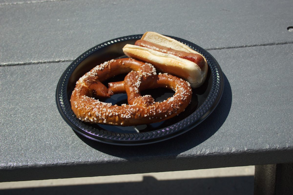 A table with a hot dog and a salted pretzel on a black plate.