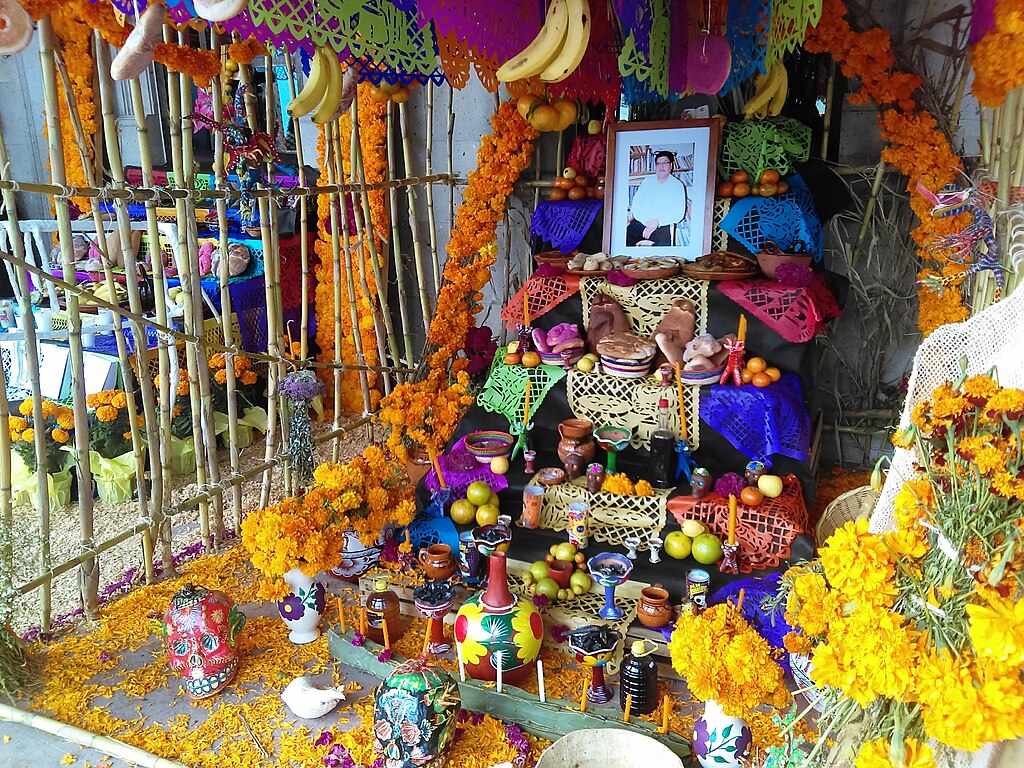 A Mexican Ofrenda surrounded by gifts and offerings. A loved one's photo is framed.