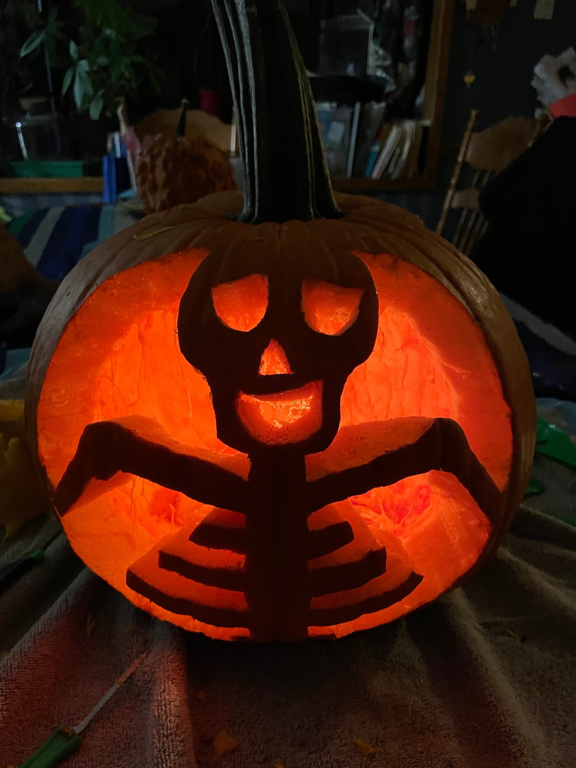 close up of an orange pumpkin carved into a skeleton-like figure with a goofy face. It is lit with a candle from the inside in a dark room sitting on a table. This is a close up of an orange pumpkin carved into a skeleton-like figure with a goofy face. It is lit with a candle from the inside in a dark room sitting on a table.