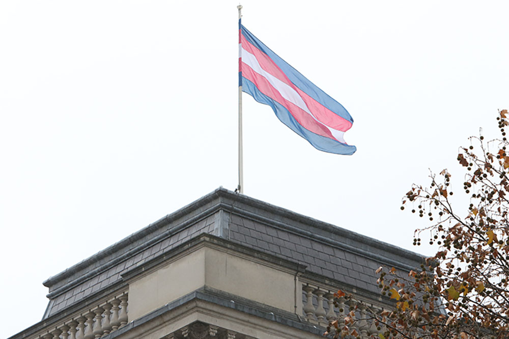 The trans flag blows in the wind as it sits atop a building.
