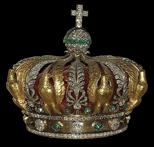 A Tiara with emerald gemstones and a miniature cross on top of it.