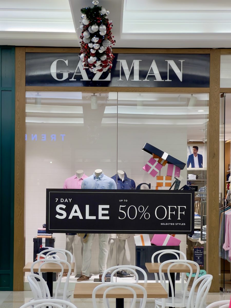 A window display of three mannequins in men's clothes with a 50% sale sign