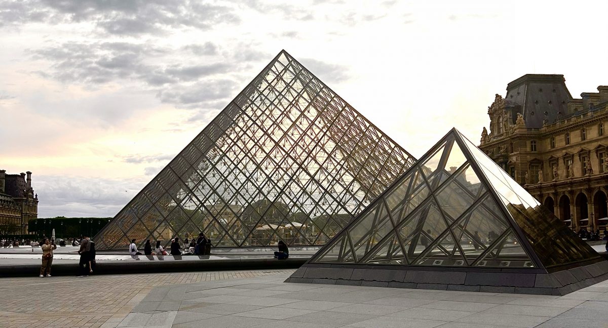 Several people standing outside of two different sized glass pyramids.