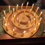 A wooden candle ring with 23 burning yellow tapers.