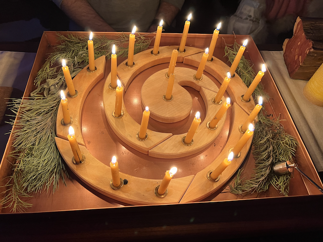 A wooden candle ring with 23 burning yellow tapers.