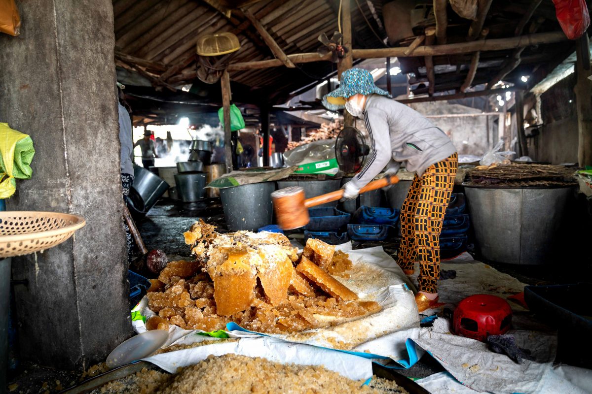 A woman crushing sugar cane with a large wooden hammer.