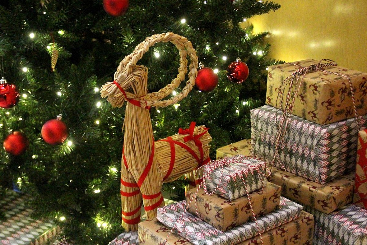 Bundles of straw fashioned into the shape of a goat, among bundles of wrapped presents in front of a Christmas tree
