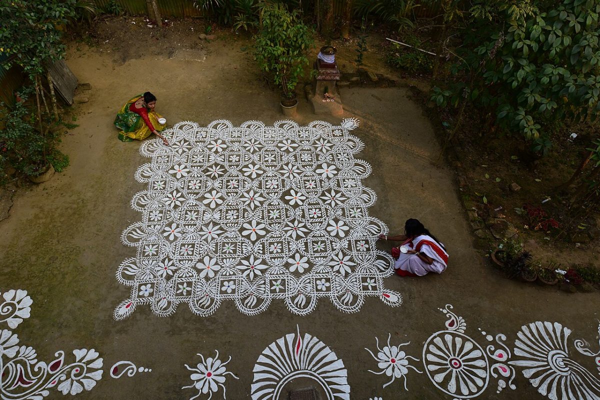 A view of two people from above marking an intricate pattern on the ground.