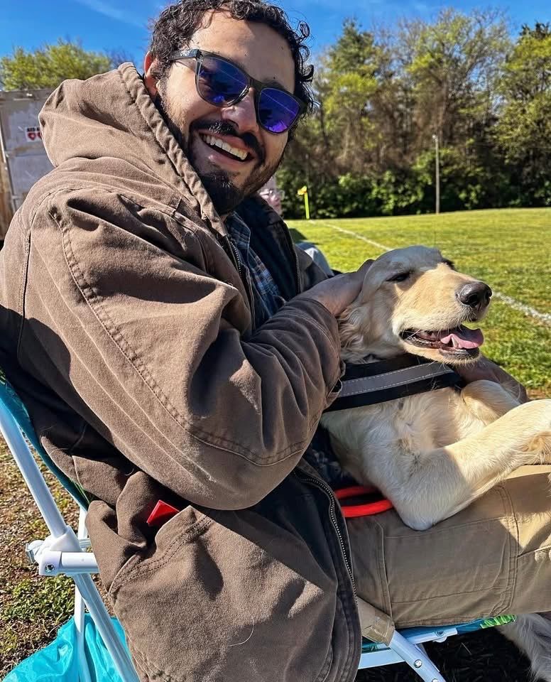 Alejandro holding a golden retriever. Alejandro is smiling.