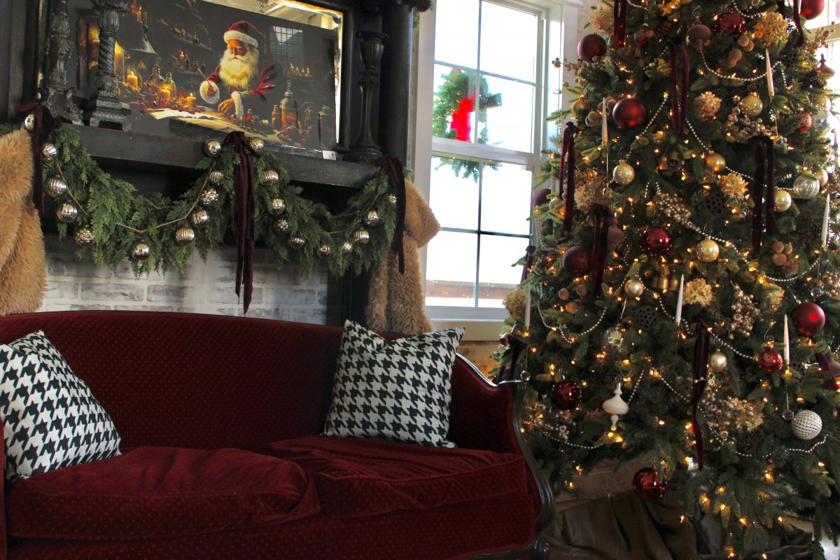 a red couch with a mantle featuring a vintage portrait of Santa Clause and a decorated red and gold Christmas Tree