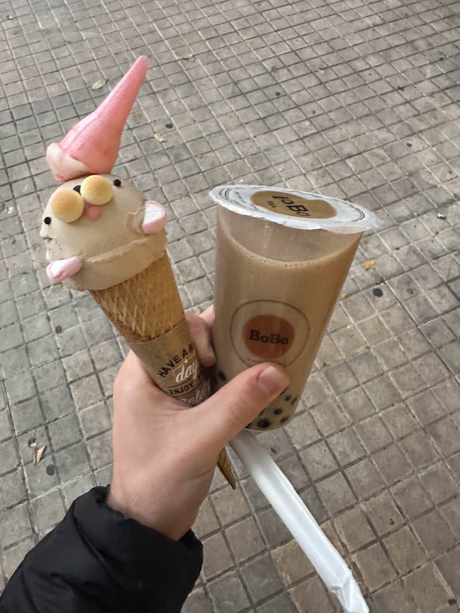 A hand holding a cone with a scoop of ice cream in the shape of a seal, as well as a cup of bubble tea