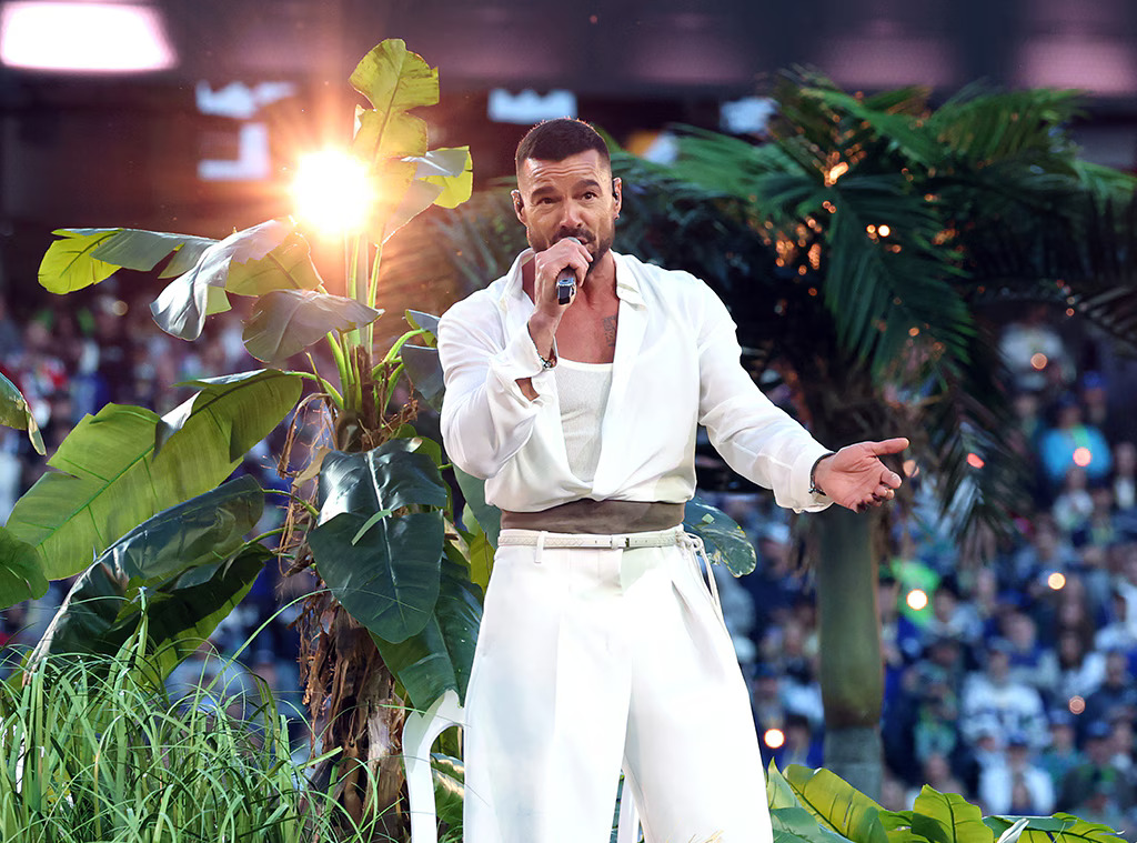 Ricky Martin singing. He stands in front of fake trees and grass.