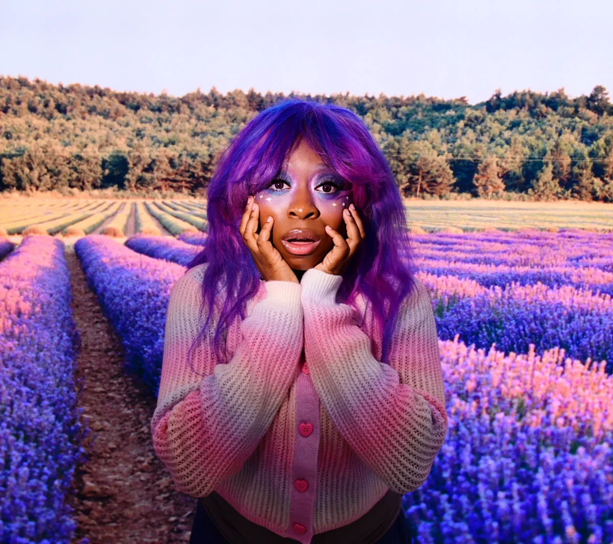 Hemlocke Springs with purple hair standing in a field of lavender in a pink cardigan