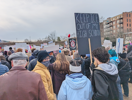 Protestors carry signs, one saying "KEEP ICE OUT OF MY HIGH SCHOOL"