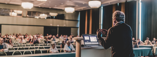 Person standing in front of a room, giving a presentation to a crowd