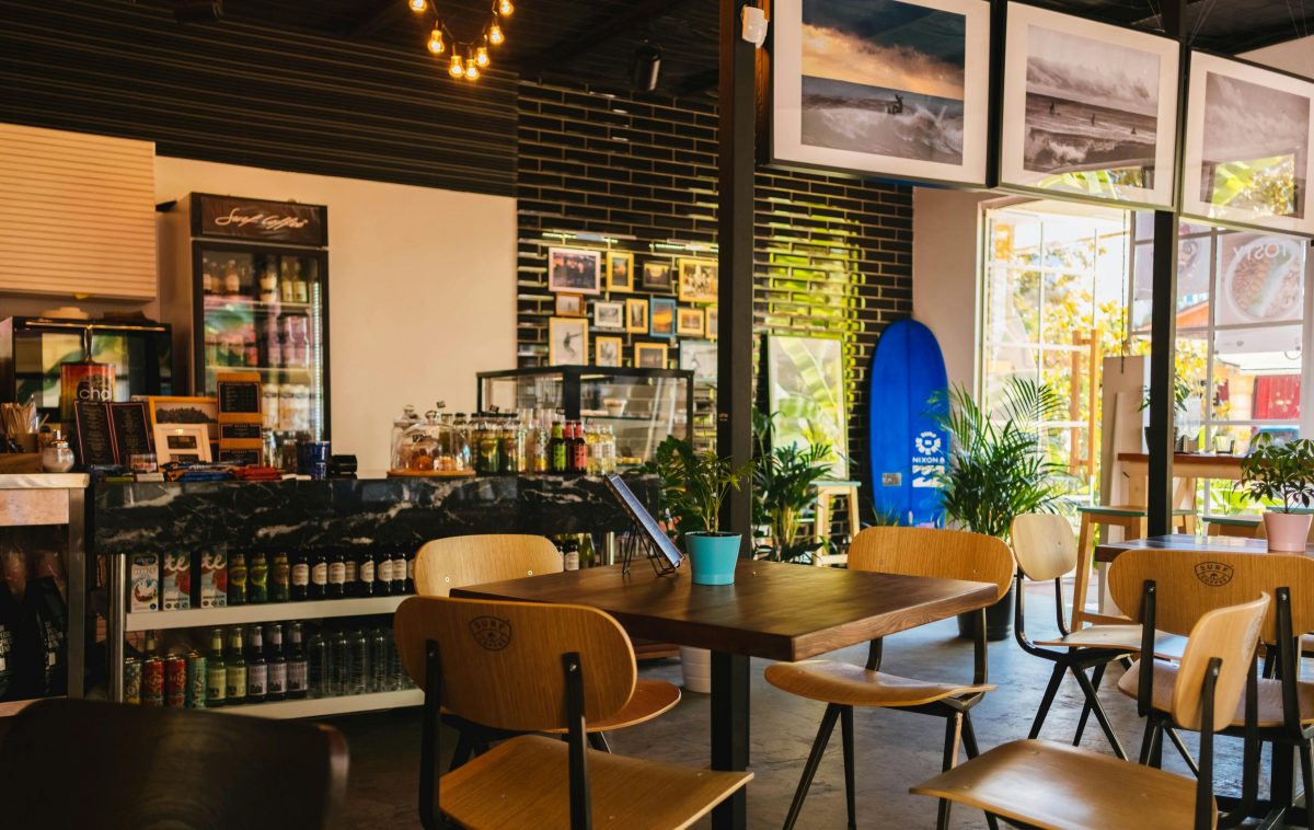 The inside of a cafe with lots of beverages on shelves, chairs, tables, and wall decorations