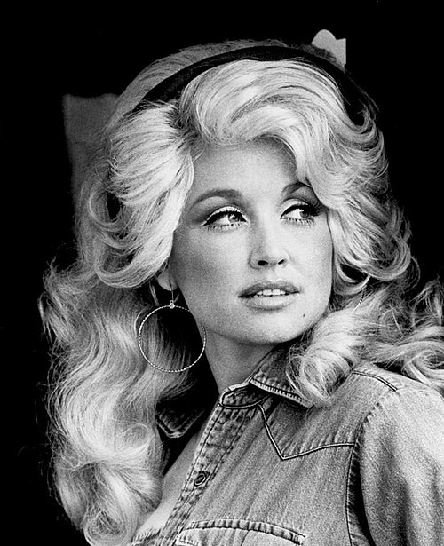 A blonde woman with heavy makeup looks over her shoulder.