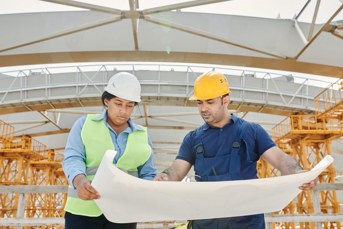 A woman and a man in construction attire looking at a blueprint in a warehouse