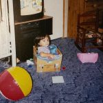 A little girl sitting in a box in a playroom
