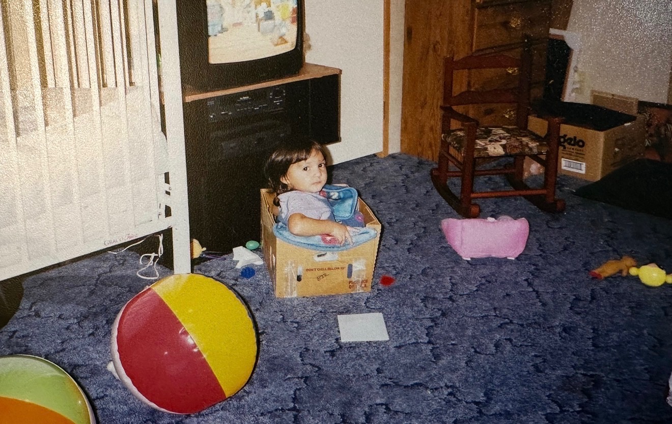 A little girl sitting in a box in a playroom